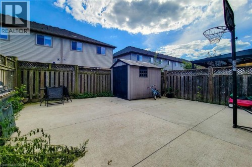 Paved backyard with a storage shed, wooden fencing, and a covered patio area - 21 Jonathon Court, Hamilton, ON 