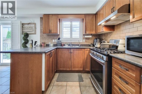 Kitchen with wood-finish cabinetry, tile backsplash, stainless steel range, and stone-finish countertops - 21 Jonathon Court, Hamilton, ON 