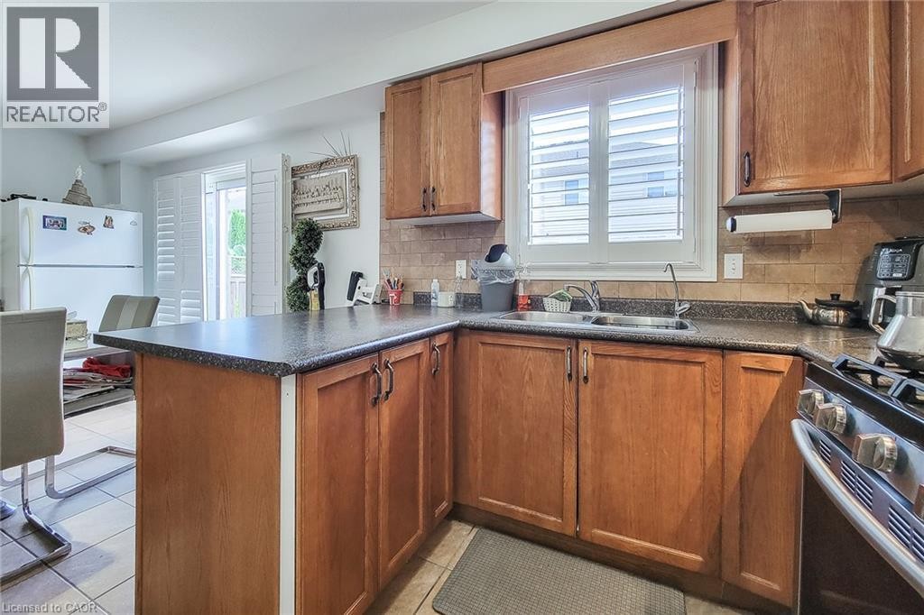 Wood-finish cabinetry with dark countertops, a tile backsplash, and a double basin sink - 21 Jonathon Court, Hamilton, ON