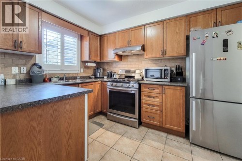 Kitchen featuring wood-finish cabinetry, stainless steel appliances, dark countertops, and a tile backsplash - 21 Jonathon Court, Hamilton, ON 