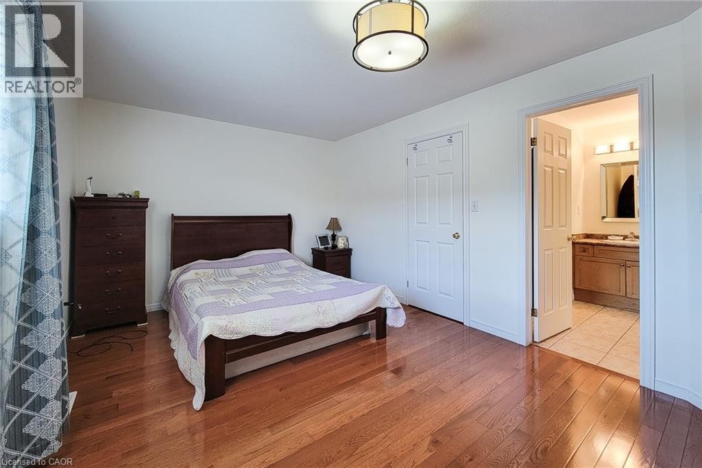 Hardwood flooring, white walls, flush mount ceiling light fixture, white interior door, and an open doorway to a bathroom with a vanity and mirror - 21 Jonathon Court, Hamilton, ON