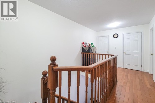 Hardwood flooring throughout the upper landing, featuring a wood spindle railing and white paneled doors - 21 Jonathon Court, Hamilton, ON 