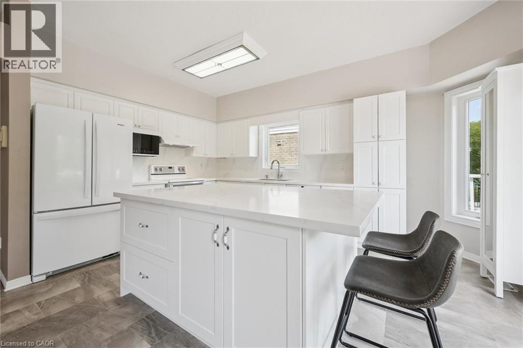 White shaker cabinetry, light-toned countertops, stone-finish flooring, recessed lighting, and a kitchen island - 426 Hidden Creek Drive, Kitchener, ON