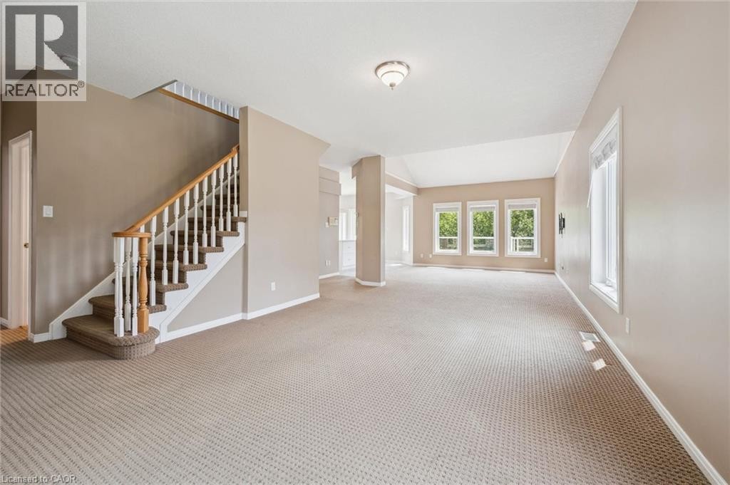 Spacious interior with neutral carpeting, a wood and white spindle staircase, multiple large windows, and a vaulted ceiling - 426 Hidden Creek Drive, Kitchener, ON