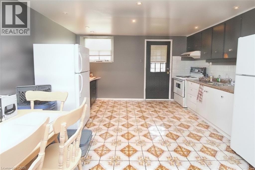 Kitchen featuring patterned floor tiles, white base cabinetry, dark wall-mounted cabinetry, a white range, and a white refrigerator - 355 Macnab Street N, Hamilton, ON