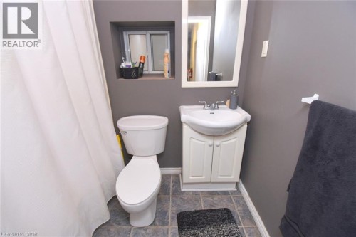 White toilet with a built-in storage niche, a single-sink vanity with a white cabinet, and tile flooring - 355 Macnab Street N, Hamilton, ON 