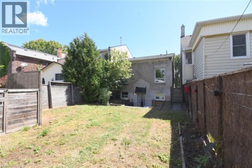 Expansive backyard featuring a sloped lawn, mature evergreen landscaping, and wood privacy fencing - 355 Macnab Street N, Hamilton, ON 