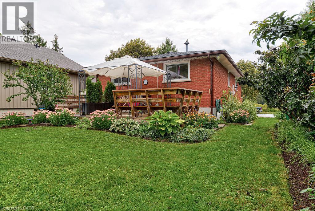 Expansive rear yard featuring a brick exterior, elevated wood deck, and diverse landscaping with mature plantings - 210 Shelley Drive, Kitchener, ON