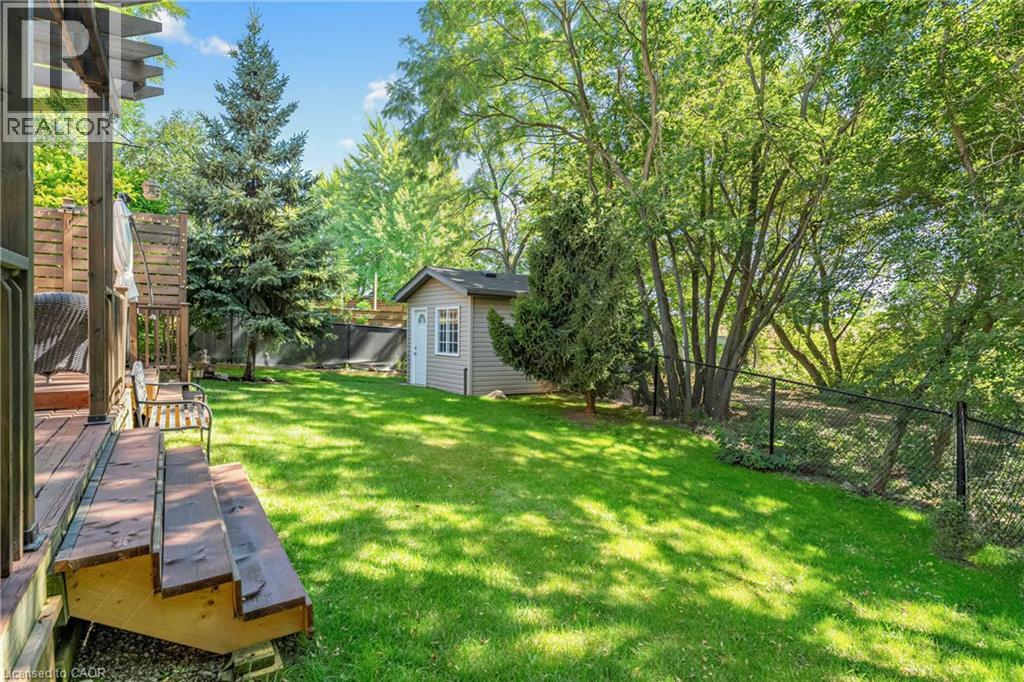 Expansive backyard featuring a manicured lawn, established trees, a wood-finish deck with steps, a black chain-link fence, and a neutral-toned storage shed - 125 Langlaw Drive, Cambridge, ON