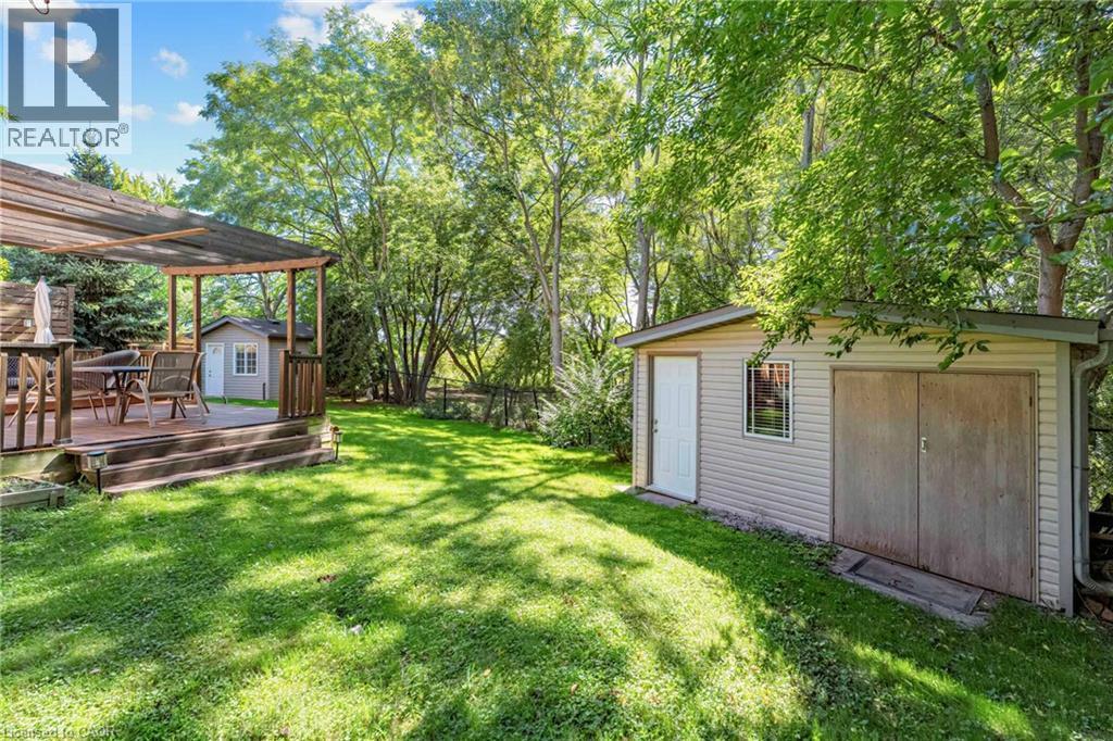 Expansive grassy backyard featuring a wood-decked patio with a pergola, mature trees, and two storage sheds - 125 Langlaw Drive, Cambridge, ON