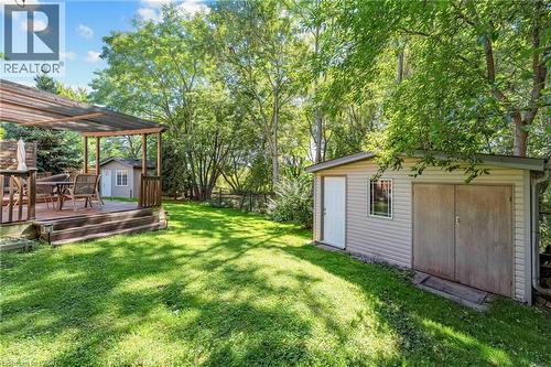 Expansive grassy backyard featuring a wood-decked patio with a pergola, mature trees, and two storage sheds - 125 Langlaw Drive, Cambridge, ON 
