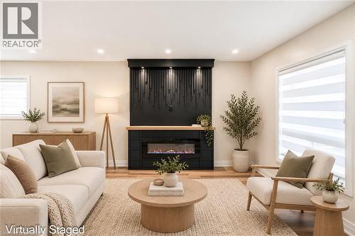Modern fireplace with a decorative mantel, wood-finish flooring, recessed lighting, and large windows - 250 Rosslyn Avenue N, Hamilton, ON 