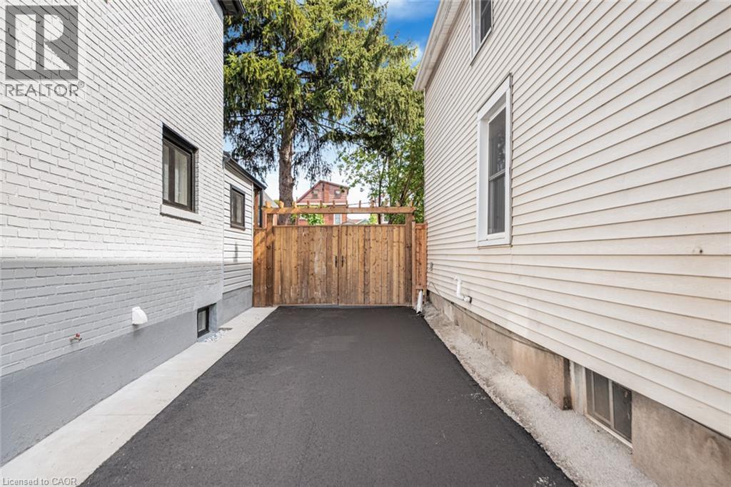Paved driveway with a wood fence and white brick exterior - 250 Rosslyn Avenue N, Hamilton, ON