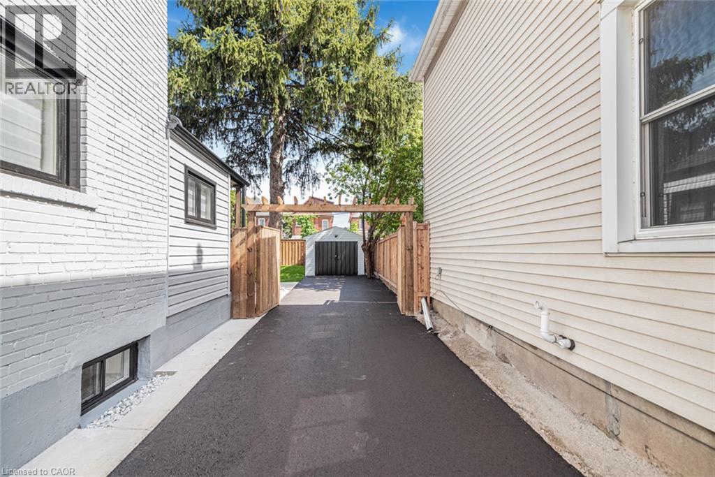 Paved driveway with wood fencing, leading to a detached garage - 250 Rosslyn Avenue N, Hamilton, ON