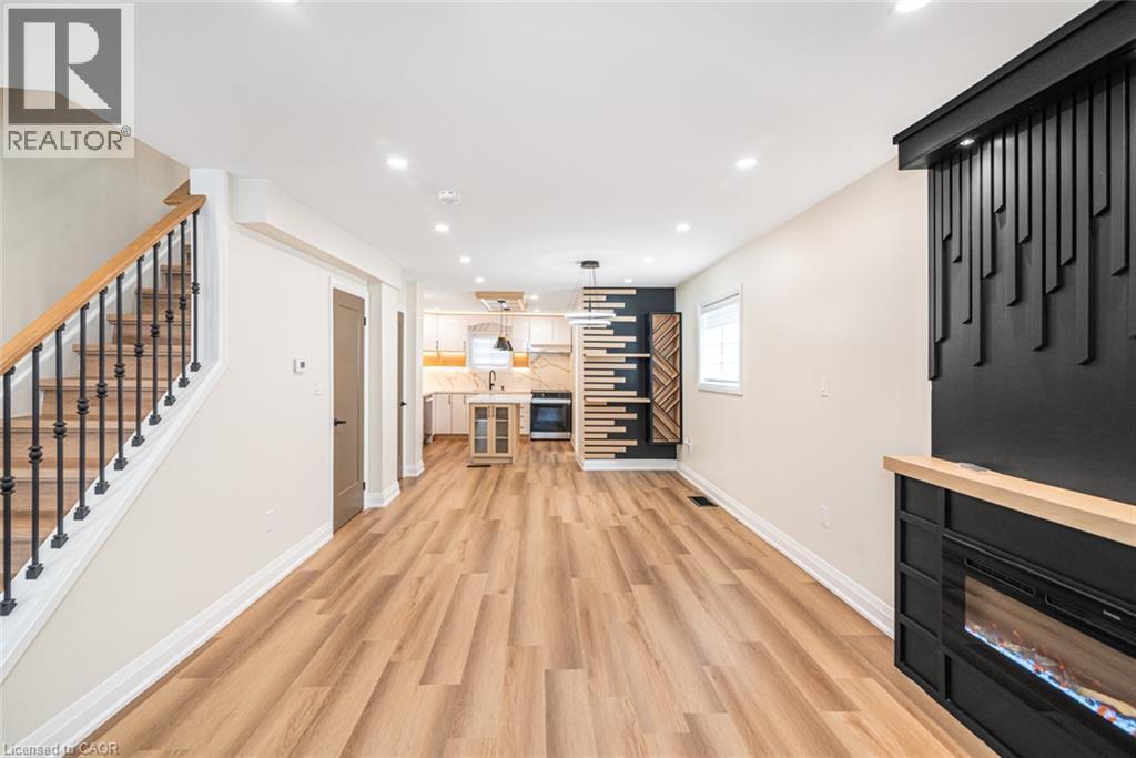 Wood-finish flooring throughout, recessed ceiling lighting, staircase with wood handrail and wrought iron spindles, built-in electric fireplace with a black surround and wood mantle, and a kitchen wit - 250 Rosslyn Avenue N, Hamilton, ON