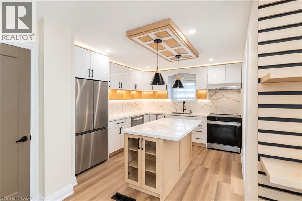 Modern kitchen featuring wood-finish flooring, white cabinetry, a central island with a light-toned countertop, and stainless steel appliances - 250 Rosslyn Avenue N, Hamilton, ON