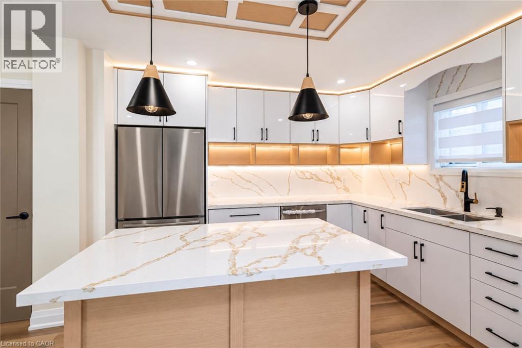 Kitchen featuring a central island with a waterfall countertop, white cabinetry, stainless steel appliances, and under-cabinet lighting - 250 Rosslyn Avenue N, Hamilton, ON