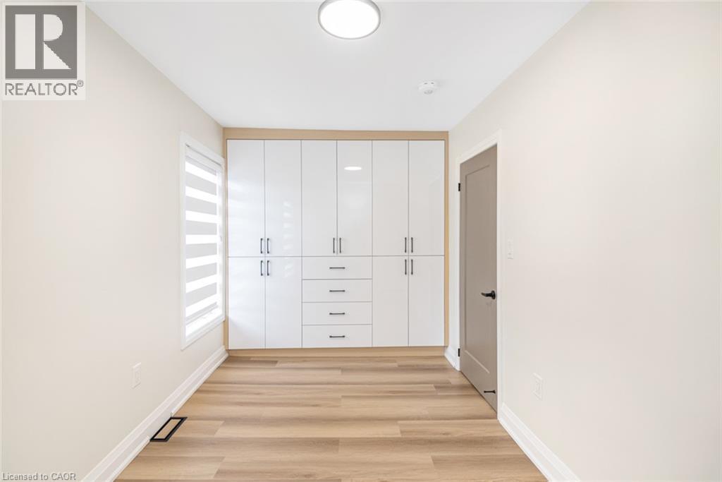 Built-in white high-gloss cabinetry with brushed nickel hardware, wood-finish flooring, a contemporary flush-mount ceiling light, and a window with horizontal blinds - 250 Rosslyn Avenue N, Hamilton, ON