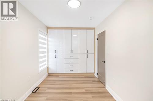 Built-in white high-gloss cabinetry with brushed nickel hardware, wood-finish flooring, a contemporary flush-mount ceiling light, and a window with horizontal blinds - 250 Rosslyn Avenue N, Hamilton, ON 