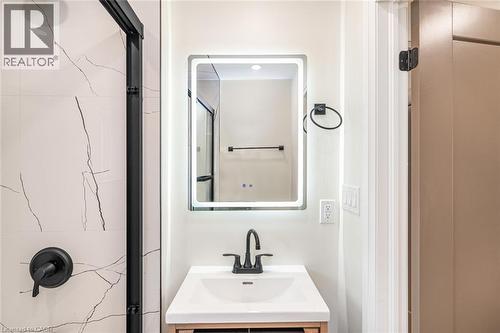 Backlit vanity mirror, black-framed shower enclosure, white tiled shower surround with dark veining, matte black shower fixtures, and a vanity with an integrated sink - 250 Rosslyn Avenue N, Hamilton, ON 