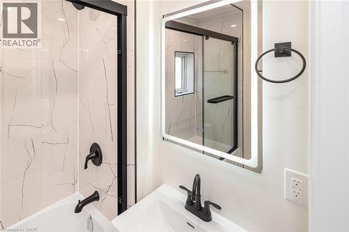 Bathroom featuring a white bathtub, black-framed shower enclosure, backlit vanity mirror, and black plumbing fixtures - 250 Rosslyn Avenue N, Hamilton, ON 