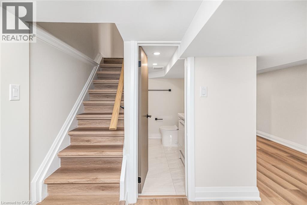 Wood-finish stairs with a light wood handrail, white trim, and light wall tones - 250 Rosslyn Avenue N, Hamilton, ON