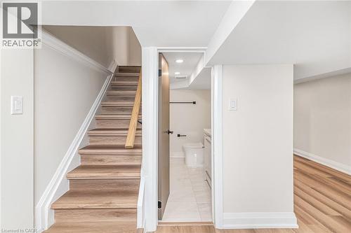 Wood-finish stairs with a light wood handrail, white trim, and light wall tones - 250 Rosslyn Avenue N, Hamilton, ON 