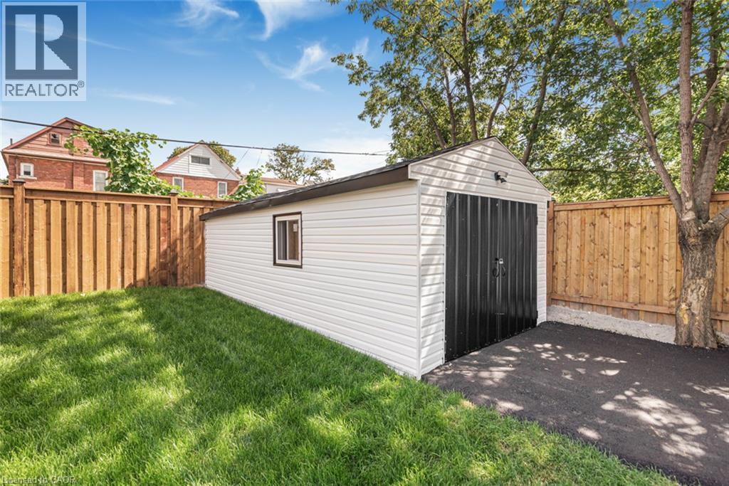 Detached garage with white vinyl siding, black panel garage door, and a single window - 250 Rosslyn Avenue N, Hamilton, ON