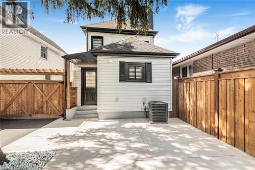 Rear exterior featuring light-colored siding, concrete patio, dark-framed window with shutters, and a wooden privacy fence - 250 Rosslyn Avenue N, Hamilton, ON 
