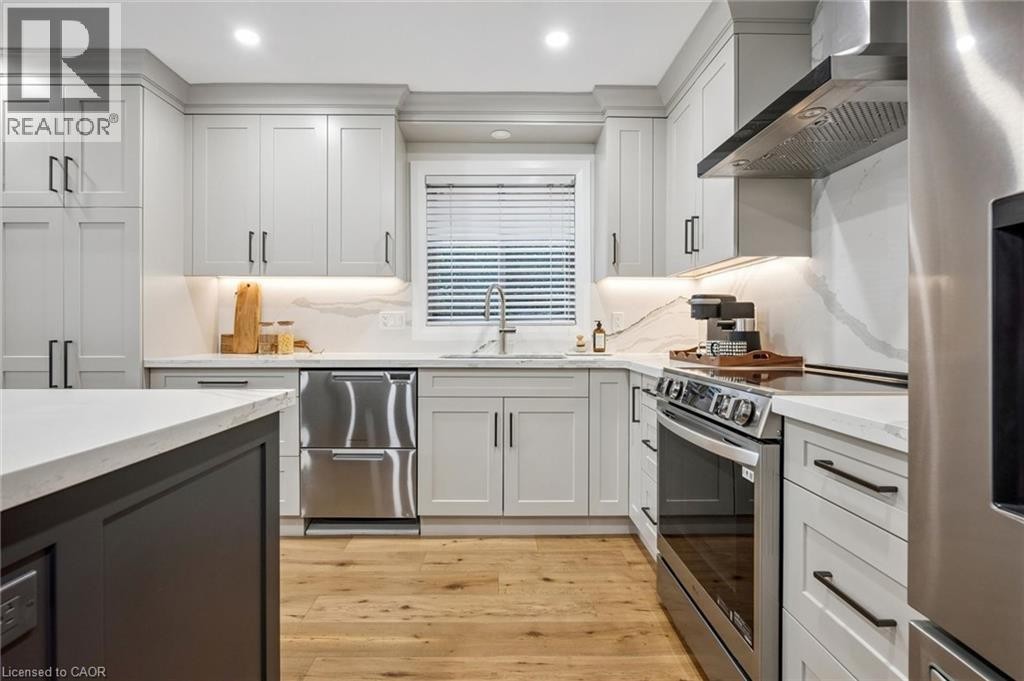 Contemporary kitchen featuring light gray cabinetry, stainless steel appliances, wood-finish flooring, and light-toned countertops with a matching backsplash - 1261 Stephenson Drive, Burlington, ON