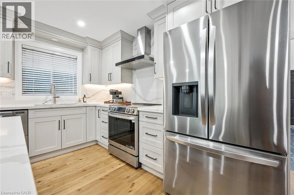 Modern kitchen featuring light-toned cabinetry with dark hardware, stainless steel appliances, quartz countertops with a matching backsplash, and wood-finish flooring - 1261 Stephenson Drive, Burlington, ON