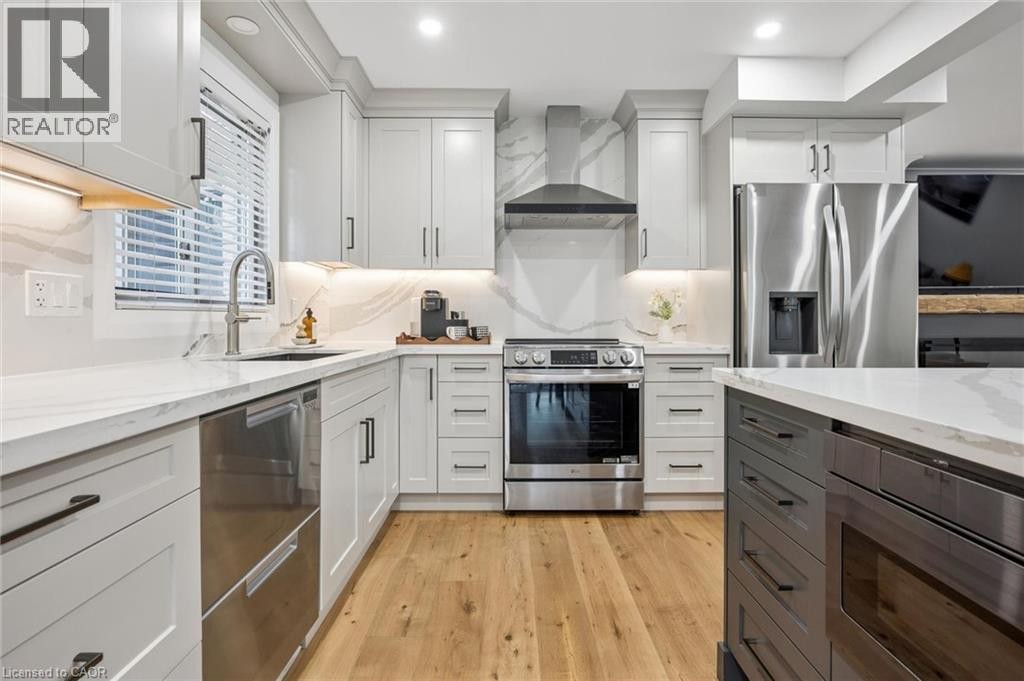 Light-toned wood-finish flooring, white cabinetry with matte black hardware, stainless steel appliances, white countertops, and a white backsplash with veining - 1261 Stephenson Drive, Burlington, ON