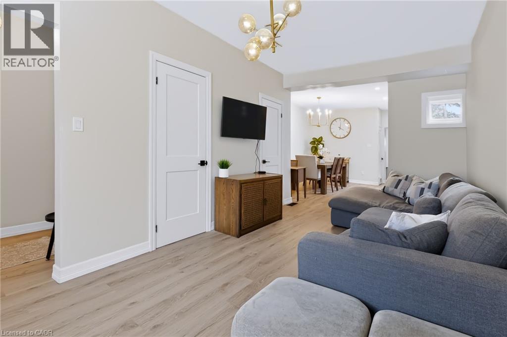 Light wood-finish flooring extends throughout the living area, complemented by a contemporary chandelier and white trim - 34 Baillie Street, Hamilton, ON