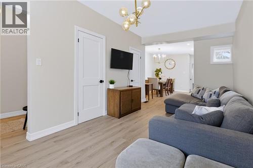 Light wood-finish flooring extends throughout the living area, complemented by a contemporary chandelier and white trim - 34 Baillie Street, Hamilton, ON 