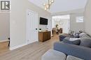 Light wood-finish flooring extends throughout the living area, complemented by a contemporary chandelier and white trim - 34 Baillie Street, Hamilton, ON 