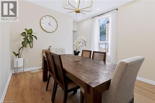 Dining area featuring wood-finish flooring, a contemporary chandelier, neutral wall paint, and a double-hung window - 34 Baillie Street, Hamilton, ON 