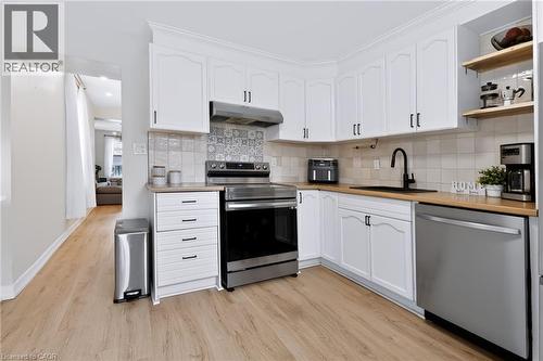 White cabinetry, wood-finish countertops, stainless steel appliances, open shelving, and a patterned tile backsplash - 34 Baillie Street, Hamilton, ON 