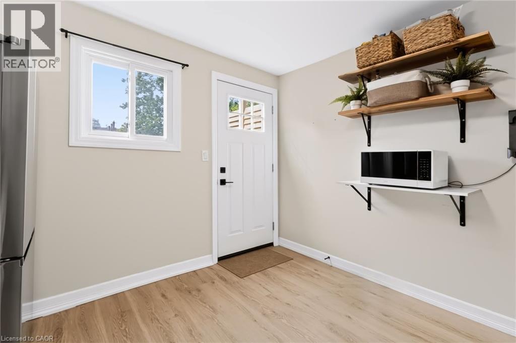 Light wood-finish flooring, white trim, and a white paneled door with multi-pane window - 34 Baillie Street, Hamilton, ON