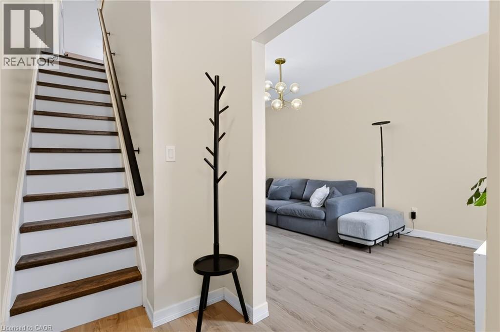 Wood-finish flooring, staircase with dark wood treads and white risers, contemporary chandelier, and light-toned wall paint - 34 Baillie Street, Hamilton, ON