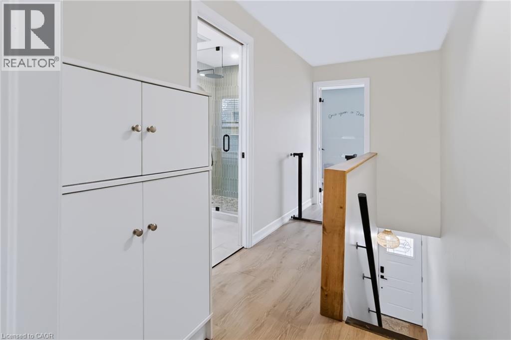 Wood-finish flooring, built-in white cabinetry, glass-enclosed shower, wood-toned stair railing, and a white paneled door - 34 Baillie Street, Hamilton, ON