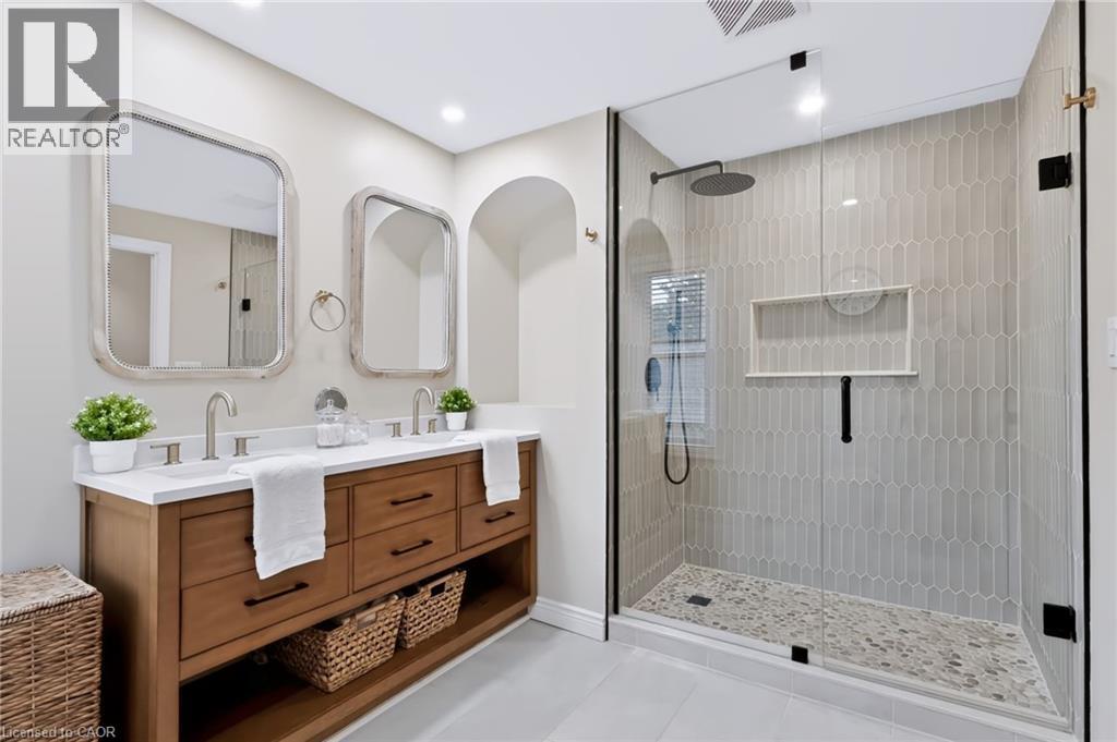 Dual vanity with wood-finish cabinetry and white countertop, complemented by two framed mirrors - 34 Baillie Street, Hamilton, ON