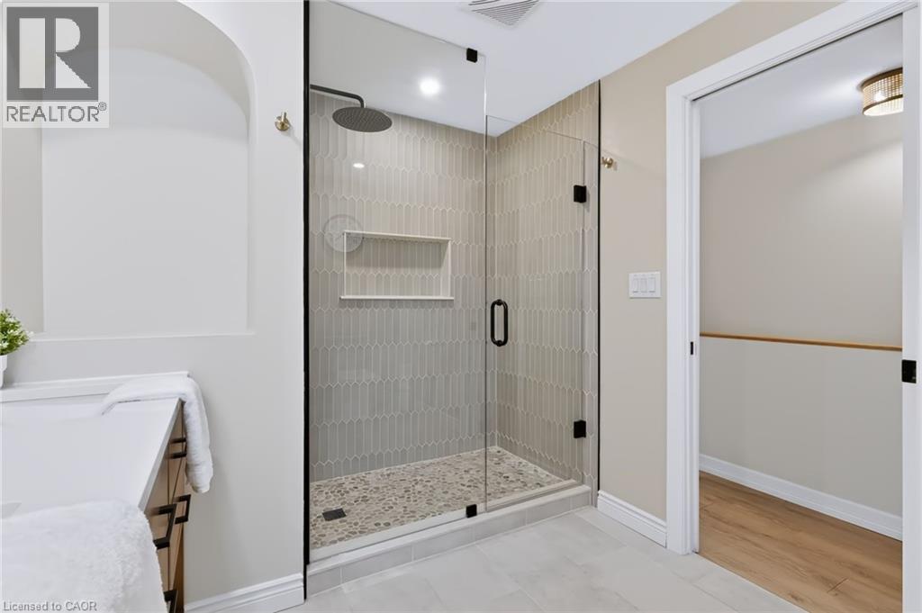 Glass-enclosed shower with a rainfall showerhead, tiled accent wall, and stone pebble flooring - 34 Baillie Street, Hamilton, ON
