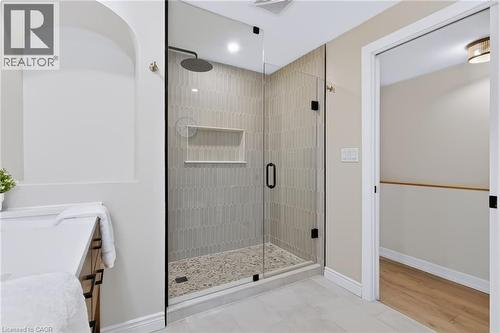 Glass-enclosed shower with a rainfall showerhead, tiled accent wall, and stone pebble flooring - 34 Baillie Street, Hamilton, ON 