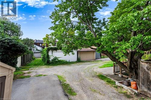 Gravel driveway with a wooden privacy fence, mature trees, and detached garage structure - 34 Baillie Street, Hamilton, ON 