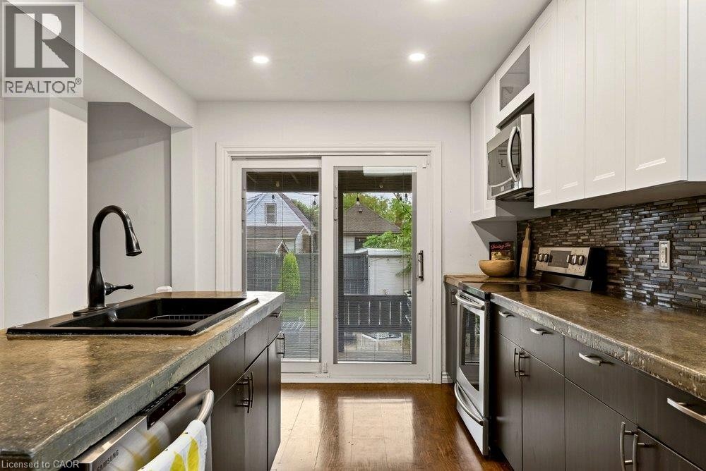 Modern kitchen featuring laminate flooring, two-tone cabinetry, and a glass tile backsplash - 136 Weir Street N, Hamilton, ON