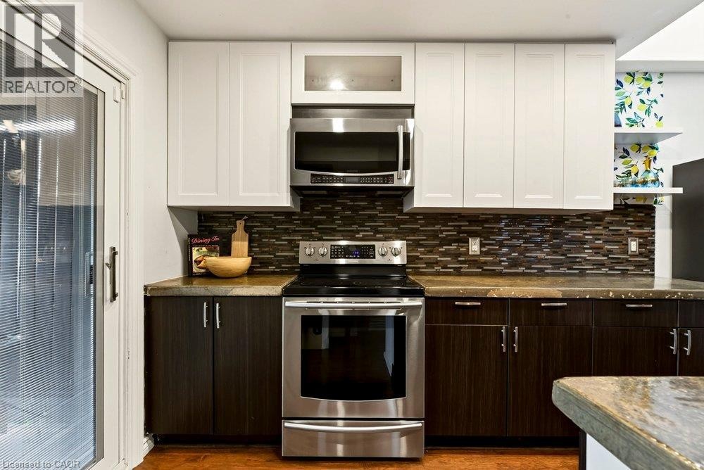 Stainless steel range and microwave, white upper cabinetry, dark wood-finish lower cabinetry, mosaic tile backsplash, and sliding glass door - 136 Weir Street N, Hamilton, ON