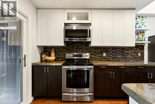 Stainless steel range and microwave, white upper cabinetry, dark wood-finish lower cabinetry, mosaic tile backsplash, and sliding glass door - 136 Weir Street N, Hamilton, ON 