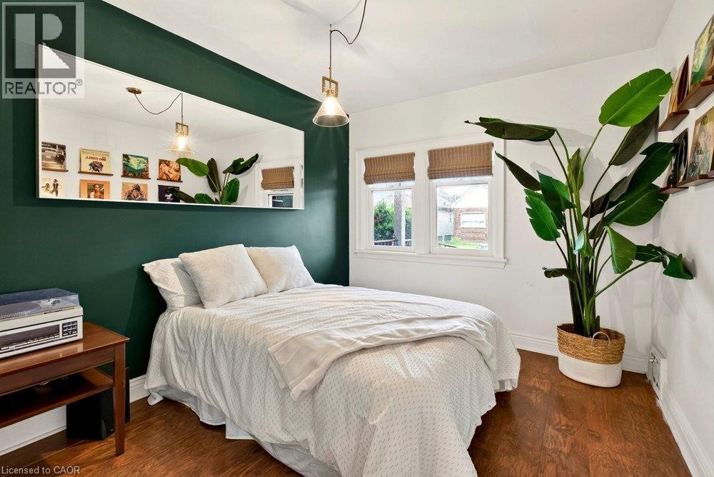 Laminate flooring throughout, dual windows with natural light, a rectangular wall-mounted mirror, and an overhead pendant light fixture - 136 Weir Street N, Hamilton, ON