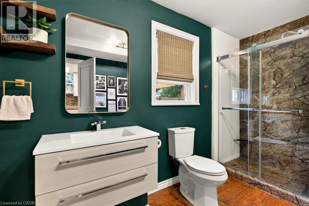 Floating vanity with an integrated rectangular sink, built-in shelving, and a glass-enclosed shower featuring natural stone-patterned walls - 136 Weir Street N, Hamilton, ON