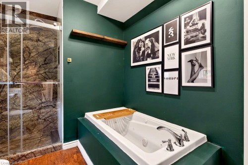 Soaking tub with chrome fixtures, glass-enclosed shower with stone-finish walls, and a wood-finish floating shelf - 136 Weir Street N, Hamilton, ON 